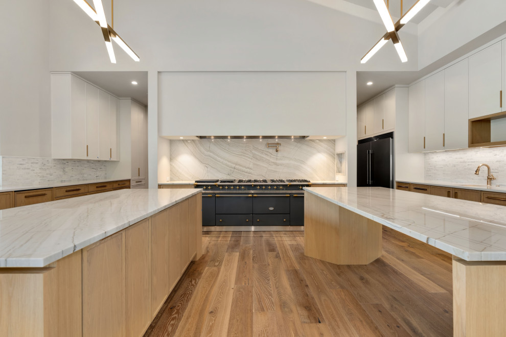 Large kitchen photo with light wood cabinets, white backsplash, stone slab backsplash, stainless steel appliances, two islands and white countertops