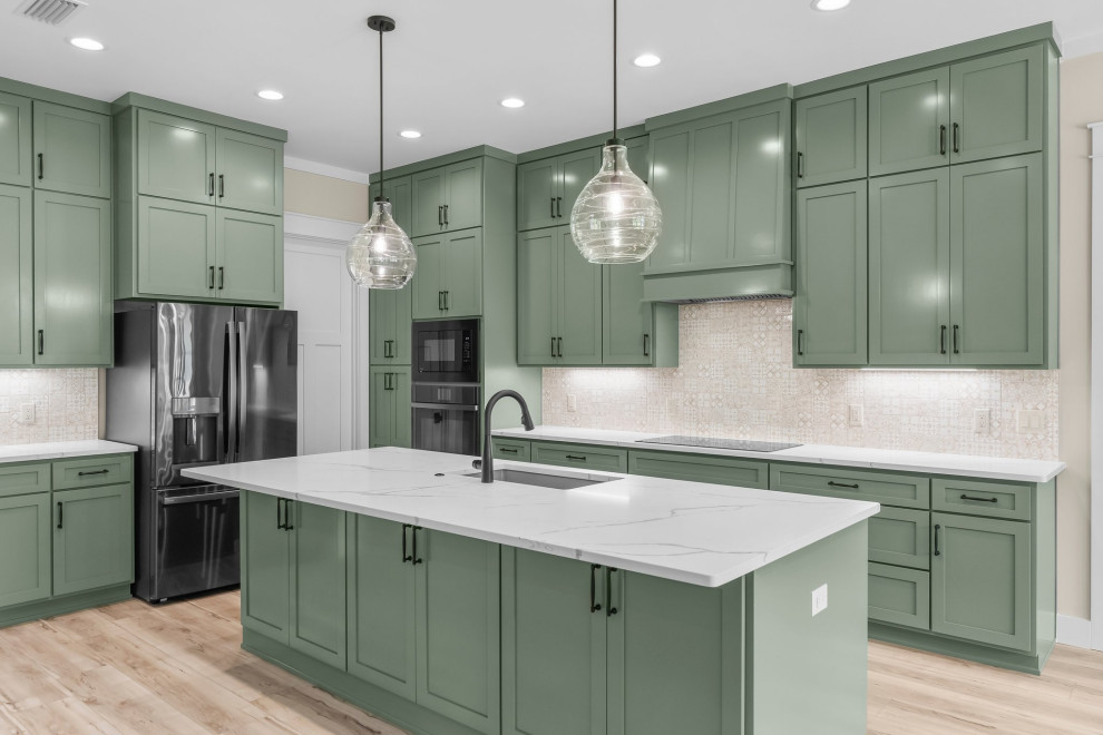 Inspiration for a craftsman l-shaped vinyl floor and beige floor open concept kitchen remodel with an undermount sink, shaker cabinets, green cabinets, quartzite countertops, beige backsplash, porcelain backsplash, stainless steel appliances, an island and white countertops