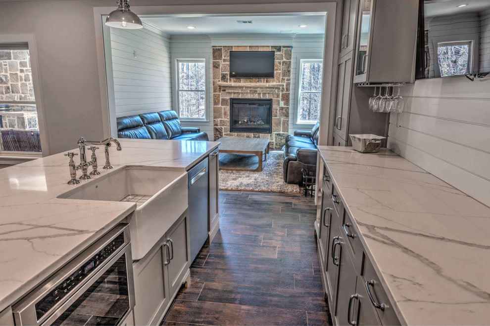 Inspiration for a mid-sized country seated home bar in Atlanta with shaker cabinets, grey cabinets, solid surface benchtops, white splashback, timber splashback, porcelain floors, brown floor and white benchtop.