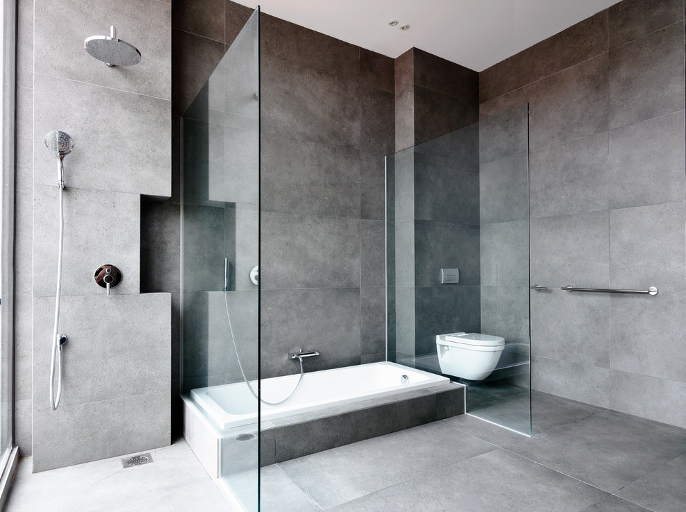Photo of a contemporary master bathroom in Singapore with an alcove tub, an open shower, a one-piece toilet, gray tile, cement tile, grey walls and concrete floors.