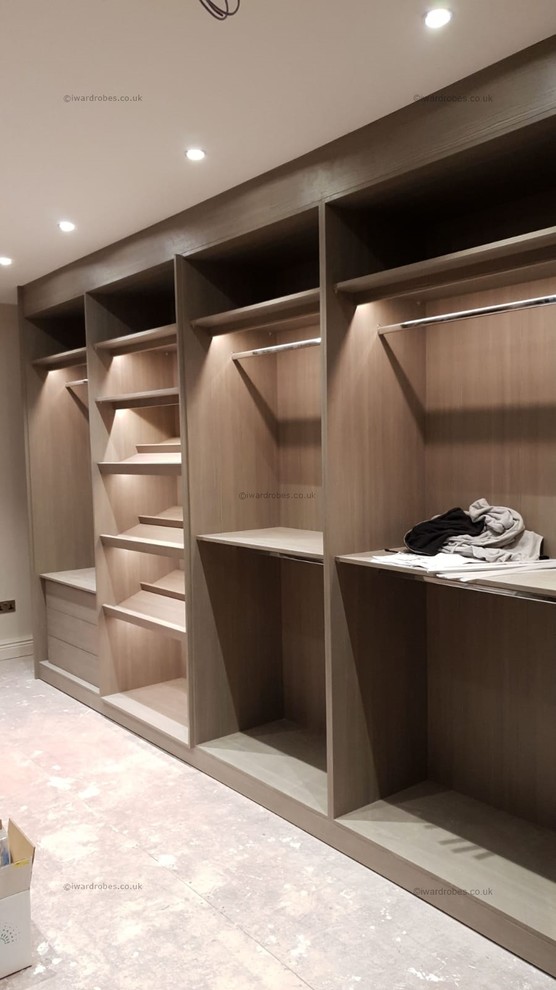 Photo of a contemporary walk-in wardrobe in London with glass-front cabinets and light wood cabinets.