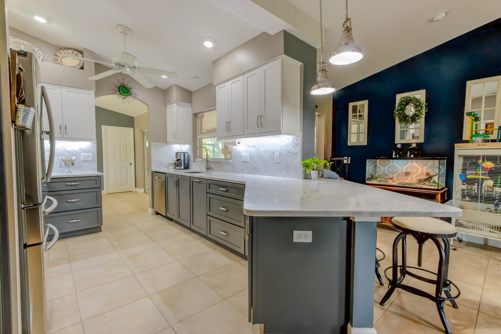 Example of a mid-sized trendy galley kitchen pantry design with an undermount sink, shaker cabinets, white cabinets, quartz countertops, white backsplash, stone slab backsplash, stainless steel appliances, a peninsula and white countertops