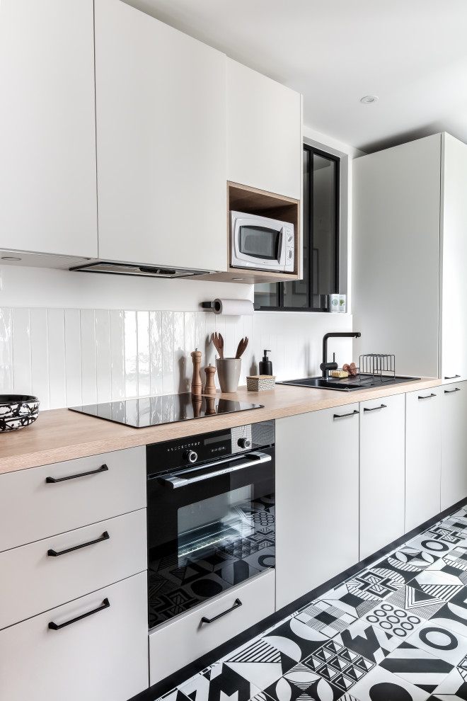 Example of a mid-sized minimalist u-shaped ceramic tile and black floor open concept kitchen design in Paris with an undermount sink, beaded inset cabinets, beige cabinets, wood countertops, white backsplash, ceramic backsplash, paneled appliances, no island and beige countertops