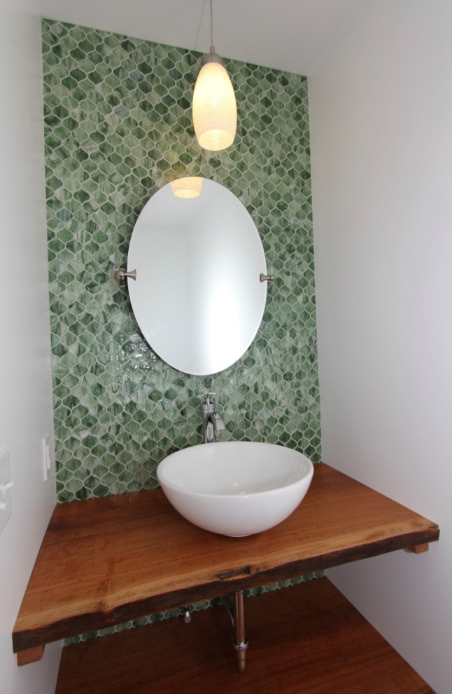 This is an example of a small country bathroom in Baltimore with medium wood cabinets, a one-piece toilet, green tile, glass tile, green walls, medium hardwood floors, a vessel sink, wood benchtops, brown floor, brown benchtops, a single vanity and a floating vanity.