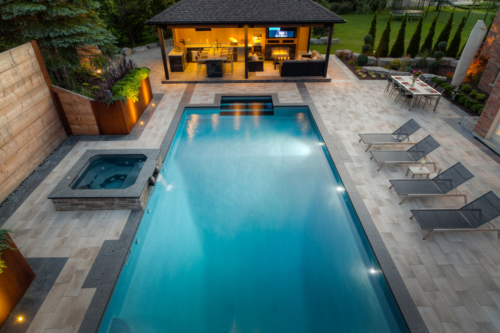Modelo de piscina moderna extra grande rectangular en patio trasero con adoquines de piedra natural