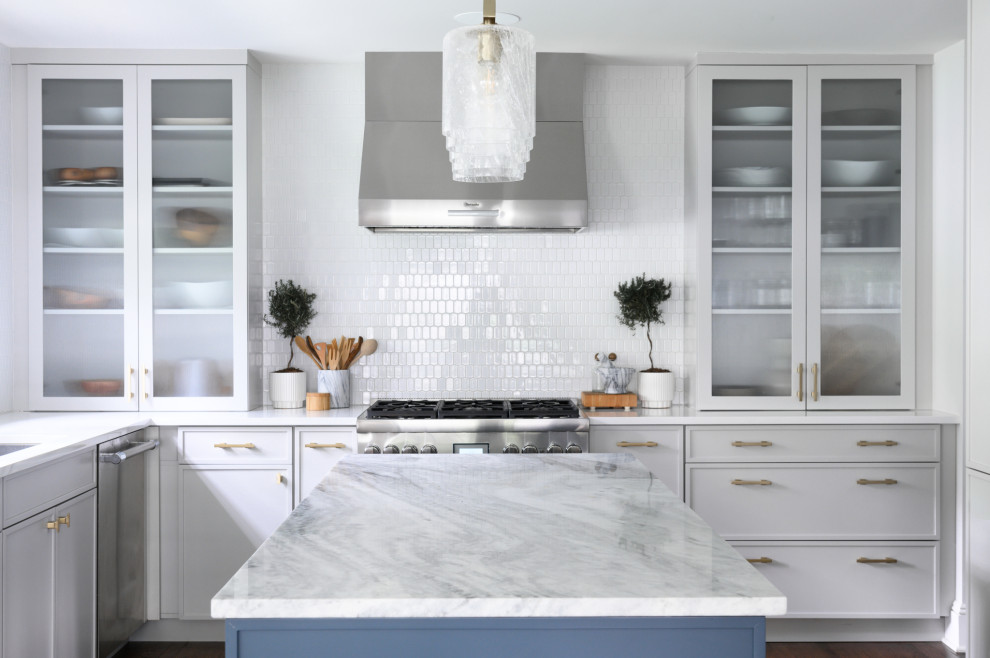 Diseño de cocina clásica renovada con salpicadero blanco, electrodomésticos de acero inoxidable, una isla, encimeras blancas, armarios tipo vitrina y salpicadero de azulejos de cerámica