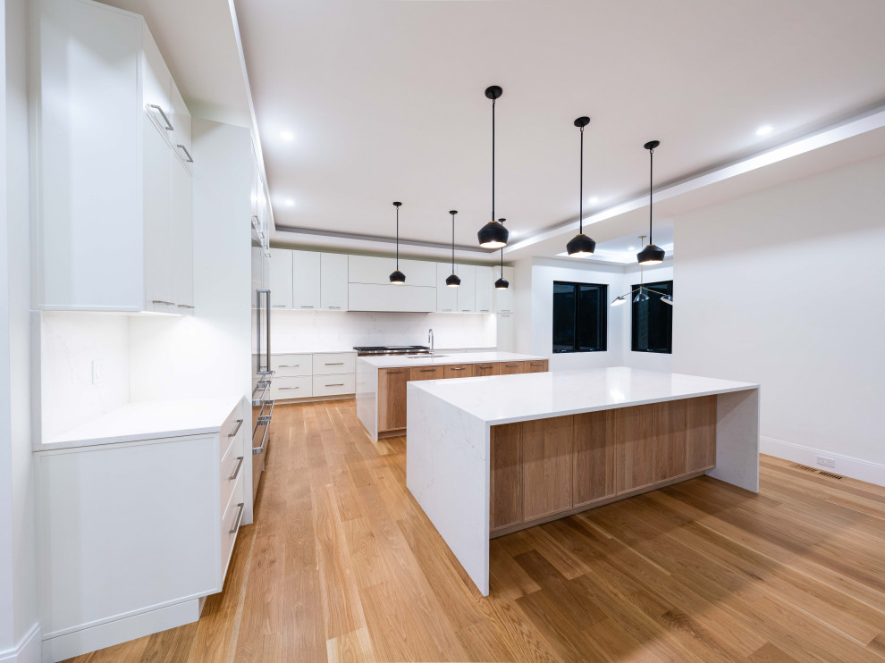 Photo of a transitional kitchen in Boston with an undermount sink, shaker cabinets, quartz benchtops, engineered quartz splashback, stainless steel appliances, light hardwood floors, multiple islands and recessed.