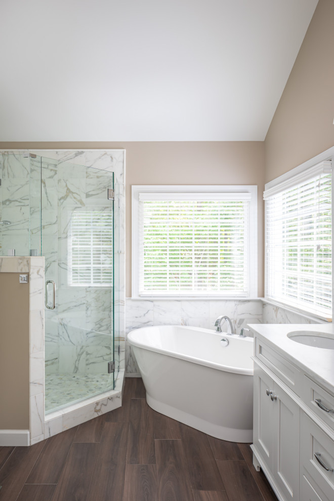 Inspiration for a mid-sized transitional master bathroom in Raleigh with recessed-panel cabinets, white cabinets, a freestanding tub, a corner shower, white tile, marble, beige walls, dark hardwood floors, an undermount sink, marble benchtops, brown floor, a hinged shower door and white benchtops.