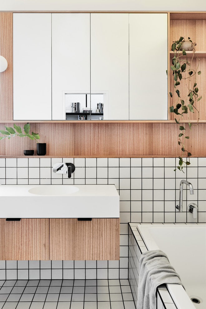 Inspiration for a mid-sized contemporary 3/4 bathroom in Melbourne with flat-panel cabinets, light wood cabinets, a drop-in tub, white tile, ceramic tile, ceramic floors, an integrated sink, engineered quartz benchtops and white floor.