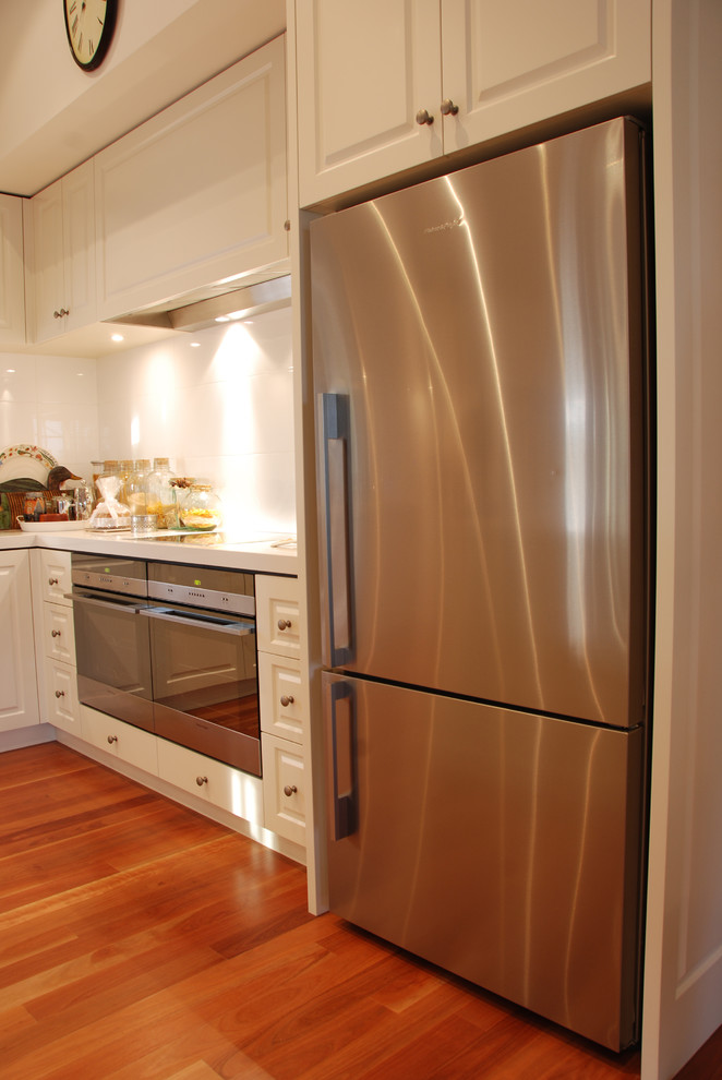 Design ideas for a large country l-shaped kitchen in Geelong with an undermount sink, recessed-panel cabinets, beige cabinets, quartz benchtops, beige splashback, glass sheet splashback, stainless steel appliances, medium hardwood floors and with island.