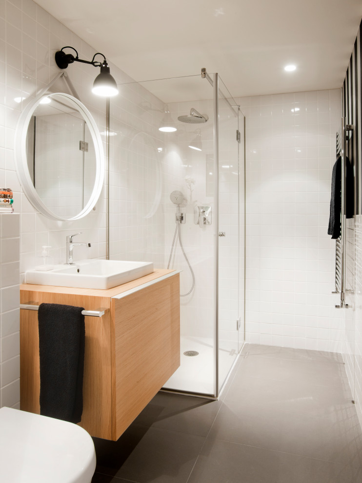 Inspiration for a mid-sized contemporary 3/4 bathroom in Other with flat-panel cabinets, light wood cabinets, a corner shower, a wall-mount toilet, white tile, porcelain floors, a vessel sink, wood benchtops, grey floor, a hinged shower door and beige benchtops.