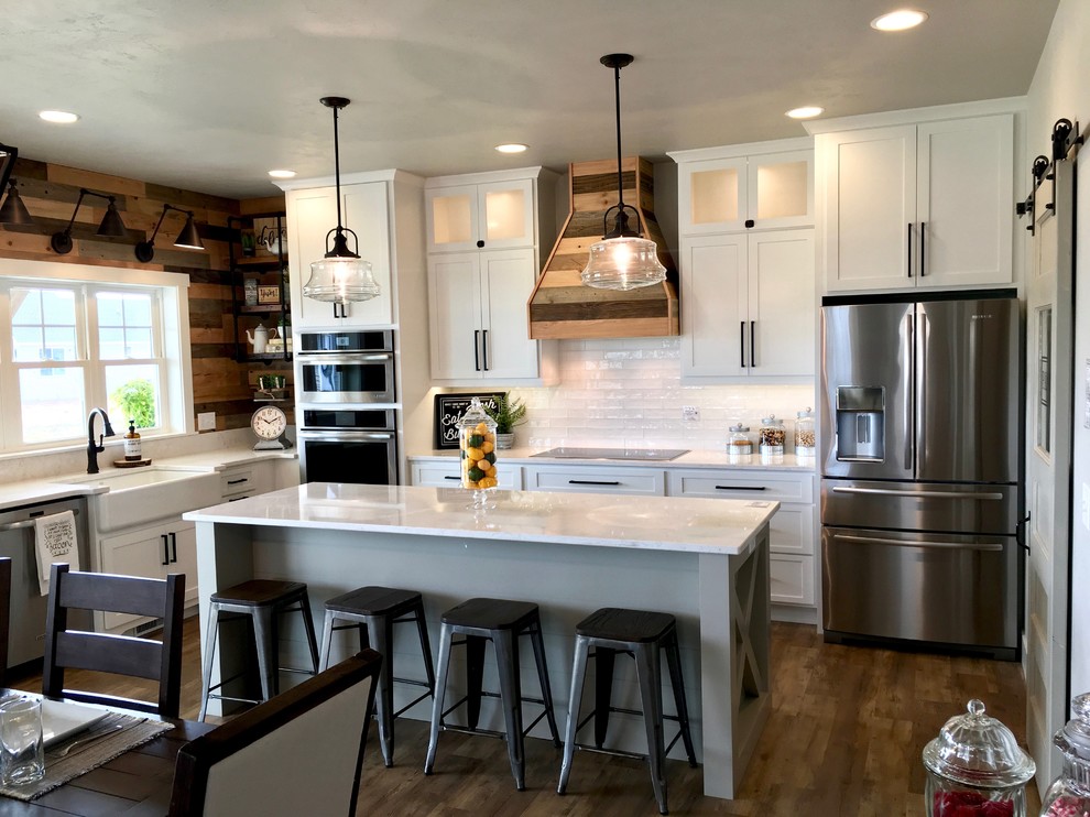 Photo of a mid-sized country u-shaped eat-in kitchen in Other with a farmhouse sink, shaker cabinets, white cabinets, marble benchtops, white splashback, subway tile splashback, stainless steel appliances, vinyl floors, with island and brown floor.