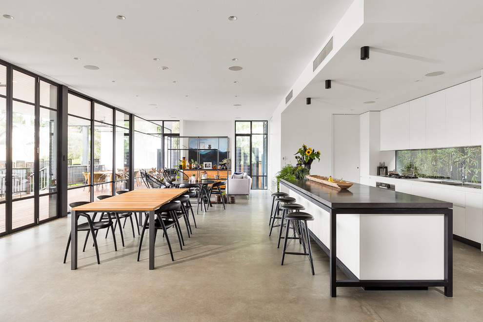 Inspiration for a contemporary galley open plan kitchen in Melbourne with flat-panel cabinets, white cabinets, window splashback, stainless steel appliances, concrete floors, with island, grey floor and grey benchtop.