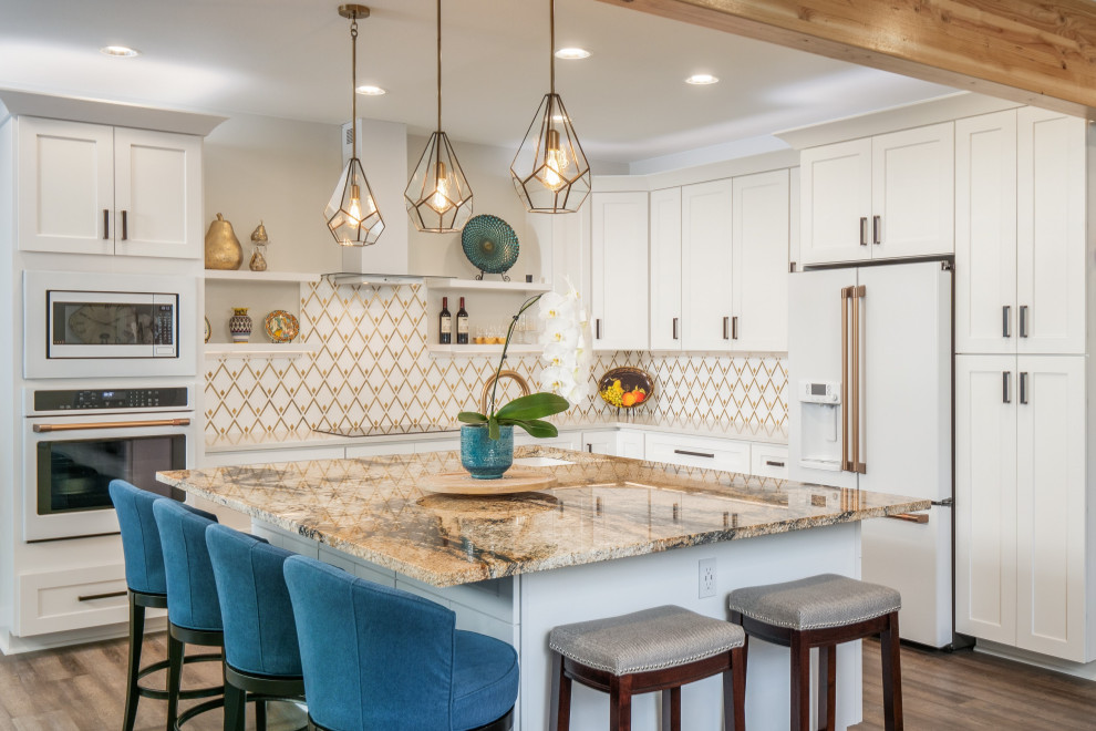 This is an example of a mid-sized transitional l-shaped open plan kitchen in Seattle with an undermount sink, shaker cabinets, white cabinets, granite benchtops, multi-coloured splashback, porcelain splashback, white appliances, vinyl floors, with island, brown floor and beige benchtop.