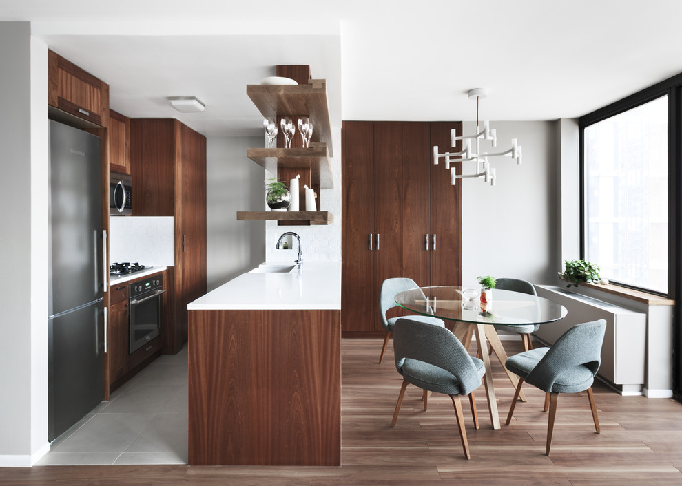 Photo of a mid-sized scandinavian galley eat-in kitchen in New York with dark wood cabinets, stainless steel appliances, a farmhouse sink, flat-panel cabinets, solid surface benchtops, porcelain floors and no island.