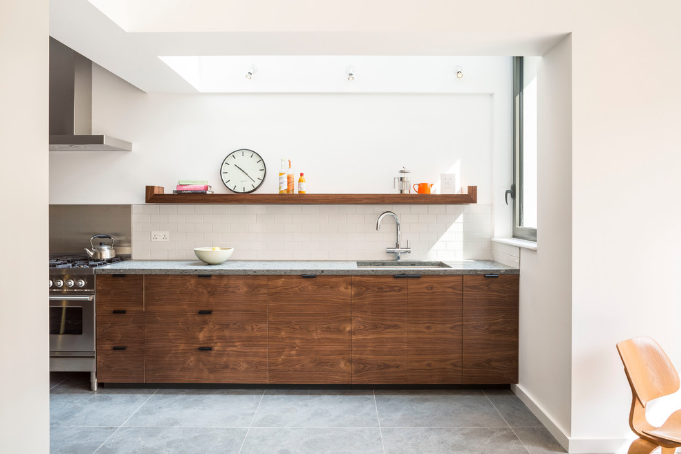 Mid-sized contemporary single-wall open plan kitchen in London with an undermount sink, flat-panel cabinets, dark wood cabinets, white splashback, subway tile splashback, stainless steel appliances, limestone floors and grey floor.