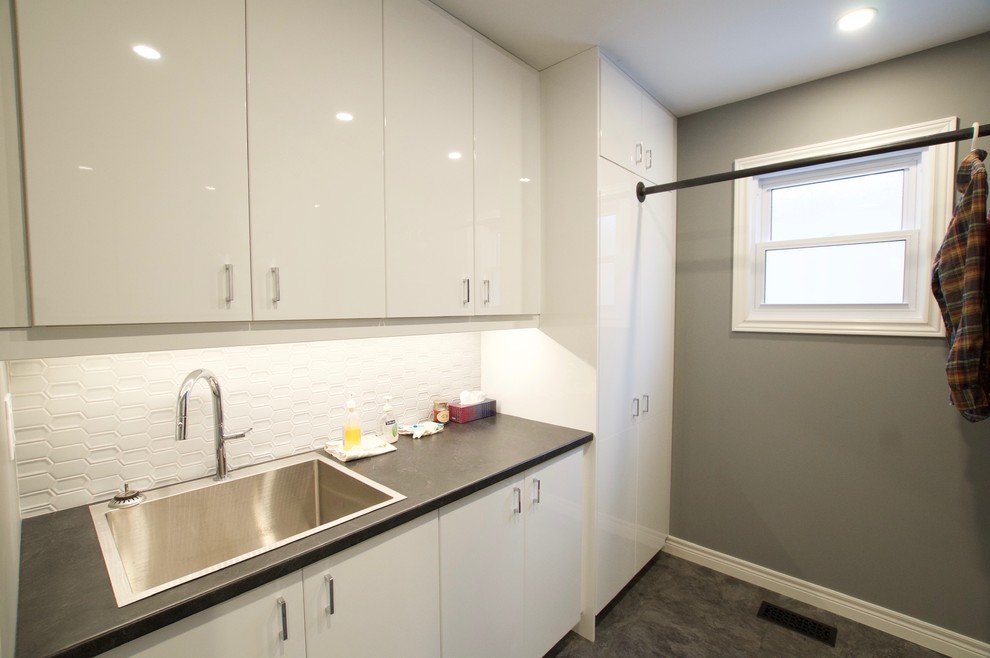 Photo of a mid-sized contemporary galley dedicated laundry room in Toronto with an utility sink, glass-front cabinets, white cabinets, laminate benchtops, grey walls, vinyl floors, a side-by-side washer and dryer, black floor and black benchtop.