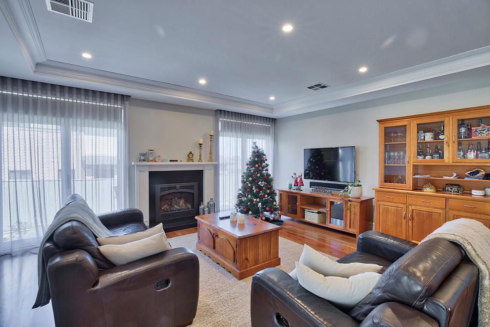Photo of a mid-sized traditional enclosed family room in Other with grey walls, medium hardwood floors, a standard fireplace, a metal fireplace surround, a wall-mounted tv and brown floor.