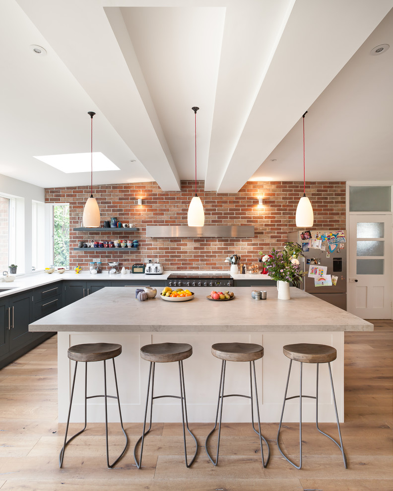 This is an example of a large transitional l-shaped eat-in kitchen in Cambridgeshire with recessed-panel cabinets, grey cabinets, solid surface benchtops, panelled appliances, with island, white benchtop, an undermount sink, red splashback, brick splashback, medium hardwood floors and brown floor.