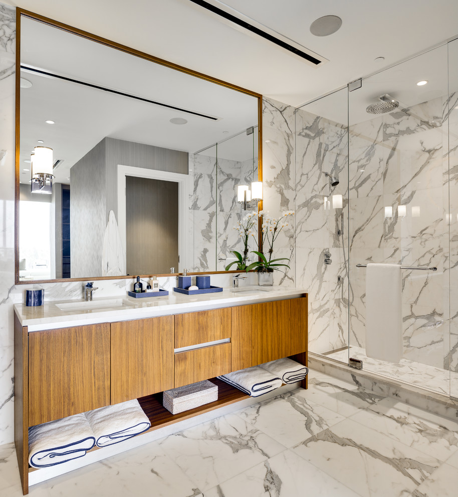 This is an example of a large contemporary master bathroom in Miami with flat-panel cabinets, medium wood cabinets, an alcove shower, white tile, marble, white walls, marble floors, an undermount sink, quartzite benchtops, white floor, a hinged shower door and white benchtops.