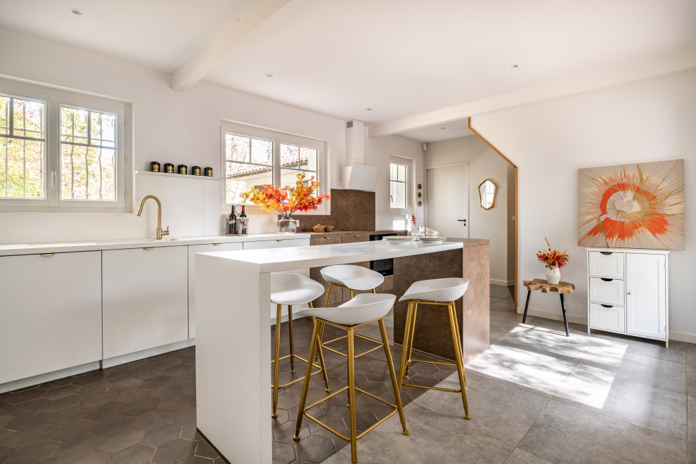 This is an example of a large contemporary single-wall open plan kitchen in Bordeaux with white cabinets, white splashback, terra-cotta floors, with island, grey floor and brown benchtop.