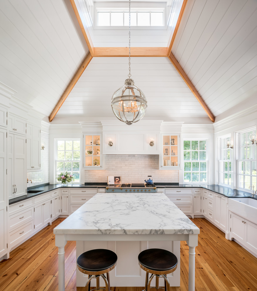 Inspiration for a cottage u-shaped medium tone wood floor enclosed kitchen remodel in Philadelphia with a farmhouse sink, shaker cabinets, white cabinets, white backsplash, subway tile backsplash, stainless steel appliances and an island