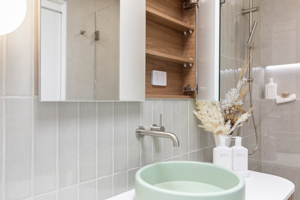 Modern inredning av ett mellanstort vit vitt badrum med dusch, med luckor med profilerade fronter, skåp i mellenmörkt trä, en öppen dusch, en toalettstol med hel cisternkåpa, grå kakel, porslinskakel, gröna väggar, klinkergolv i porslin, ett fristående handfat, bänkskiva i akrylsten, grått golv och med dusch som är öppen