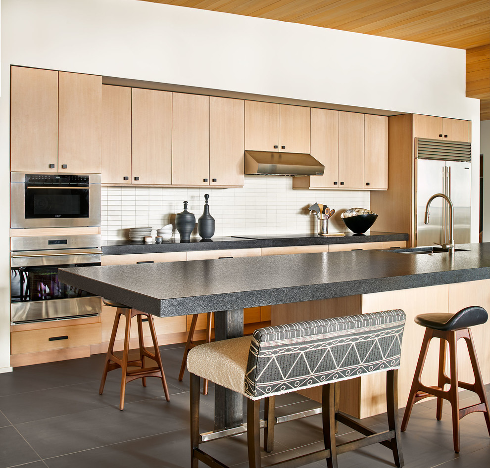Photo of a contemporary galley eat-in kitchen in Denver with an undermount sink, flat-panel cabinets, light wood cabinets, white splashback, stainless steel appliances, with island, grey floor and grey benchtop.