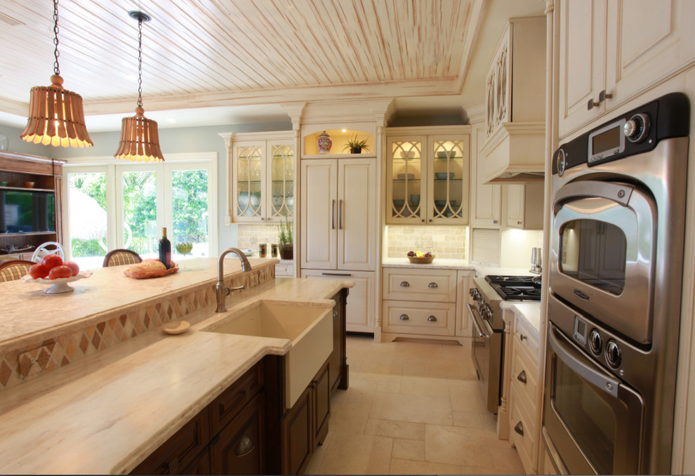 This is an example of a large traditional l-shaped eat-in kitchen in Miami with a farmhouse sink, raised-panel cabinets, white cabinets, marble benchtops, beige splashback, stone tile splashback, stainless steel appliances, ceramic floors and with island.