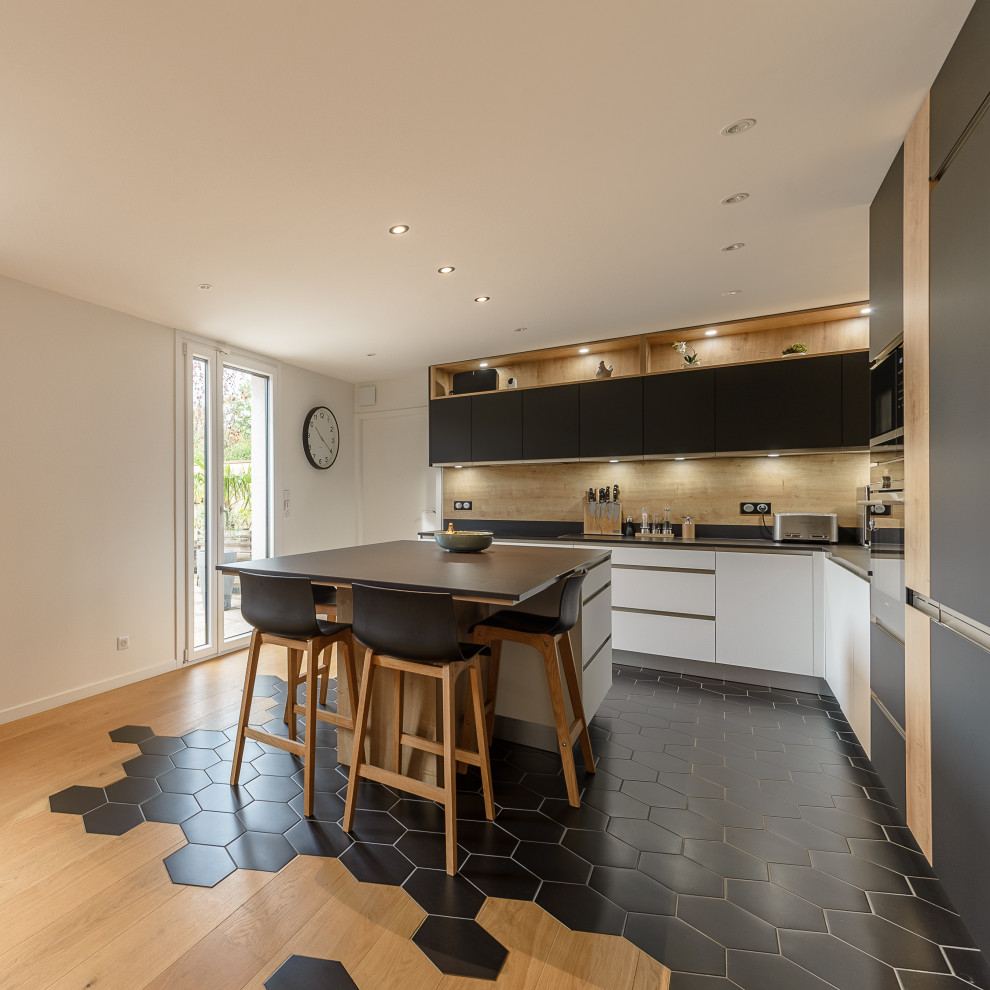 Große Moderne Wohnküche in L-Form mit Rückwand aus Holz, Küchengeräten aus Edelstahl, hellem Holzboden, Kücheninsel, schwarzem Boden und schwarzer Arbeitsplatte in Lyon