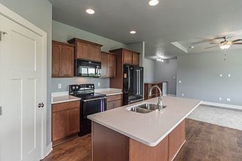 Mid-sized transitional l-shaped medium tone wood floor eat-in kitchen photo with an undermount sink, recessed-panel cabinets, medium tone wood cabinets, quartz countertops, black appliances and an island