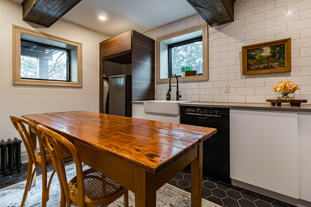 Inspiration for a mid-sized rustic u-shaped ceramic tile, black floor and exposed beam eat-in kitchen remodel in Toronto with a farmhouse sink, flat-panel cabinets, white cabinets, quartz countertops, white backsplash, subway tile backsplash, stainless steel appliances, an island and gray countertops