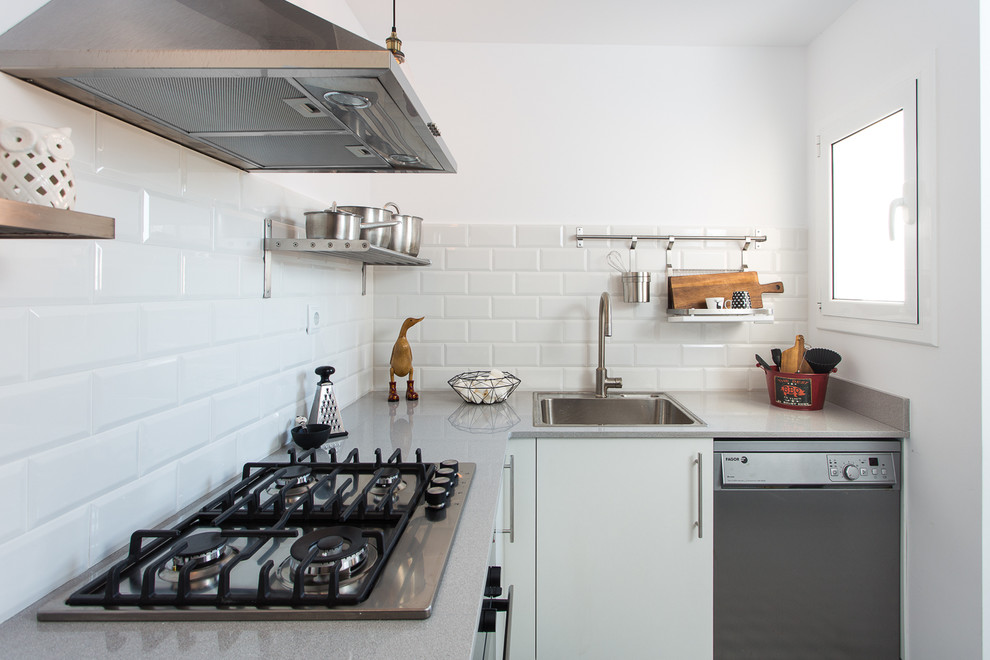 Small industrial l-shaped separate kitchen in Barcelona with a drop-in sink, flat-panel cabinets, white cabinets, solid surface benchtops, white splashback, subway tile splashback, stainless steel appliances, no island and grey benchtop.