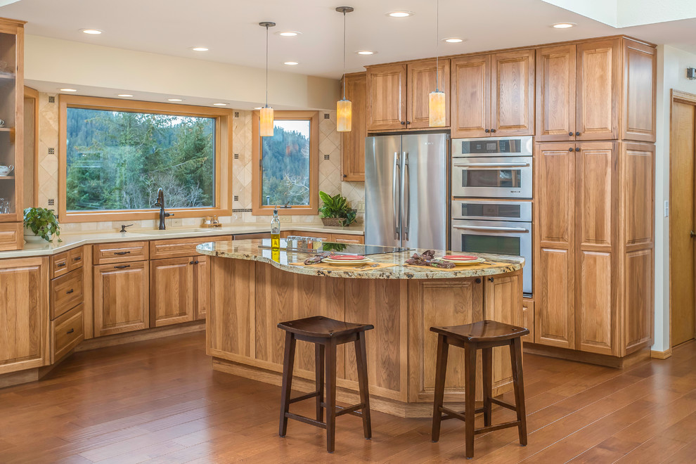 This is an example of an eclectic l-shaped eat-in kitchen in Other with an undermount sink, raised-panel cabinets, medium wood cabinets, granite benchtops, beige splashback, stone tile splashback, stainless steel appliances, medium hardwood floors and with island.