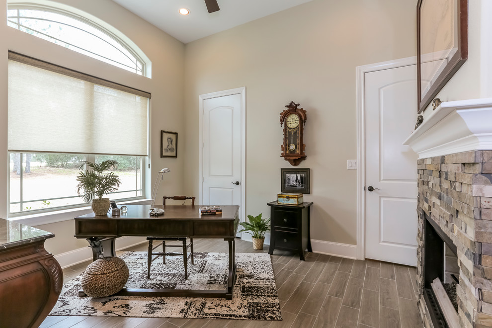 This is an example of a mid-sized transitional study room in Houston with beige walls, porcelain floors, a standard fireplace, a stone fireplace surround and a freestanding desk.