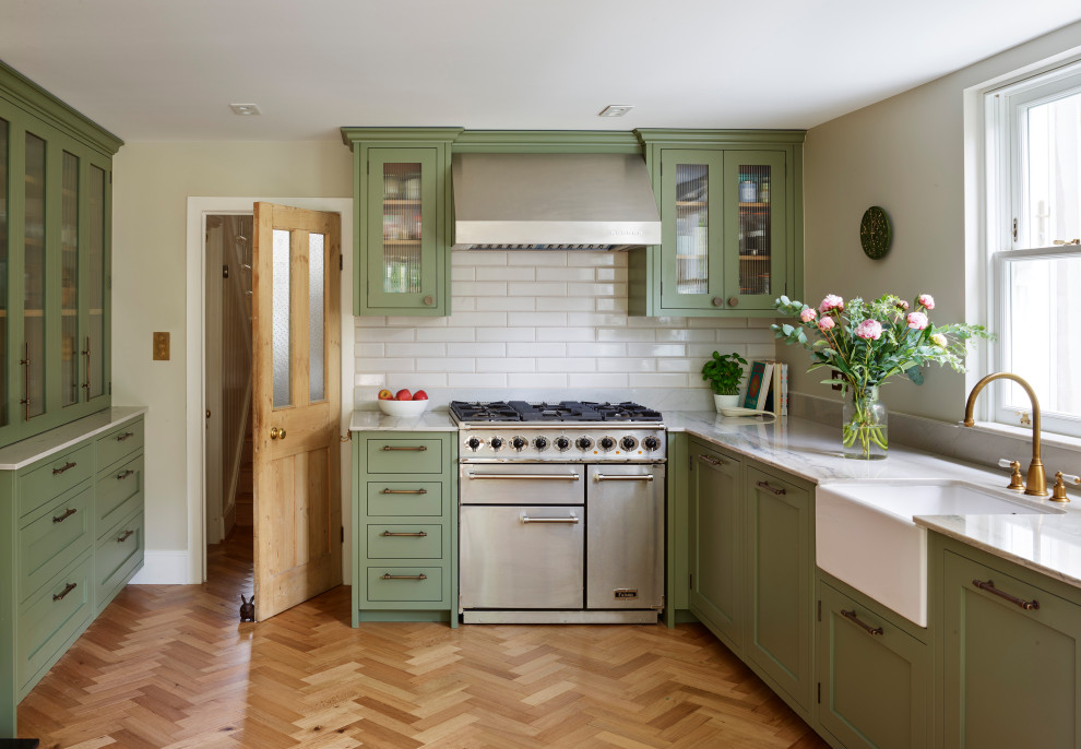 Photo of a large traditional u-shaped eat-in kitchen in Gloucestershire with a farmhouse sink, shaker cabinets, green cabinets, quartzite benchtops, white splashback, ceramic splashback, stainless steel appliances, medium hardwood floors, no island, brown floor and multi-coloured benchtop.