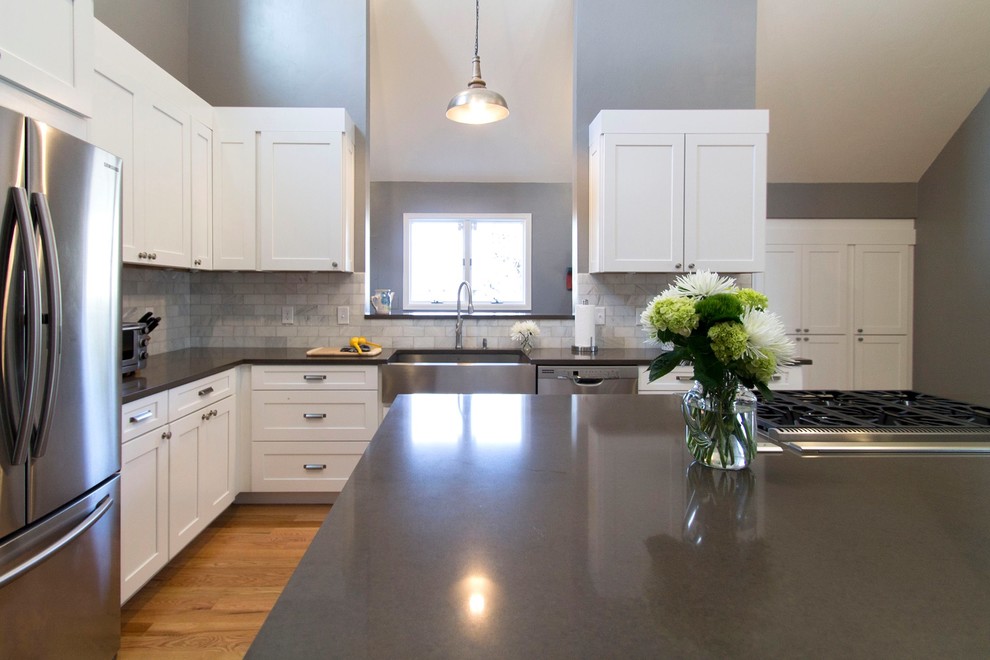 Photo of an expansive transitional l-shaped eat-in kitchen in Denver with a farmhouse sink, shaker cabinets, white cabinets, quartz benchtops, white splashback, stone tile splashback, stainless steel appliances, light hardwood floors and with island.