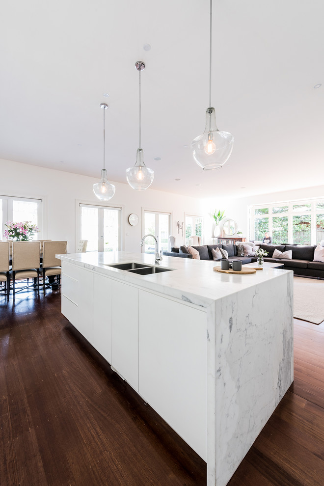 Inspiration for a mid-sized contemporary single-wall open plan kitchen in Melbourne with an undermount sink, flat-panel cabinets, white cabinets, marble benchtops, white splashback, subway tile splashback, stainless steel appliances, dark hardwood floors, with island and brown floor.