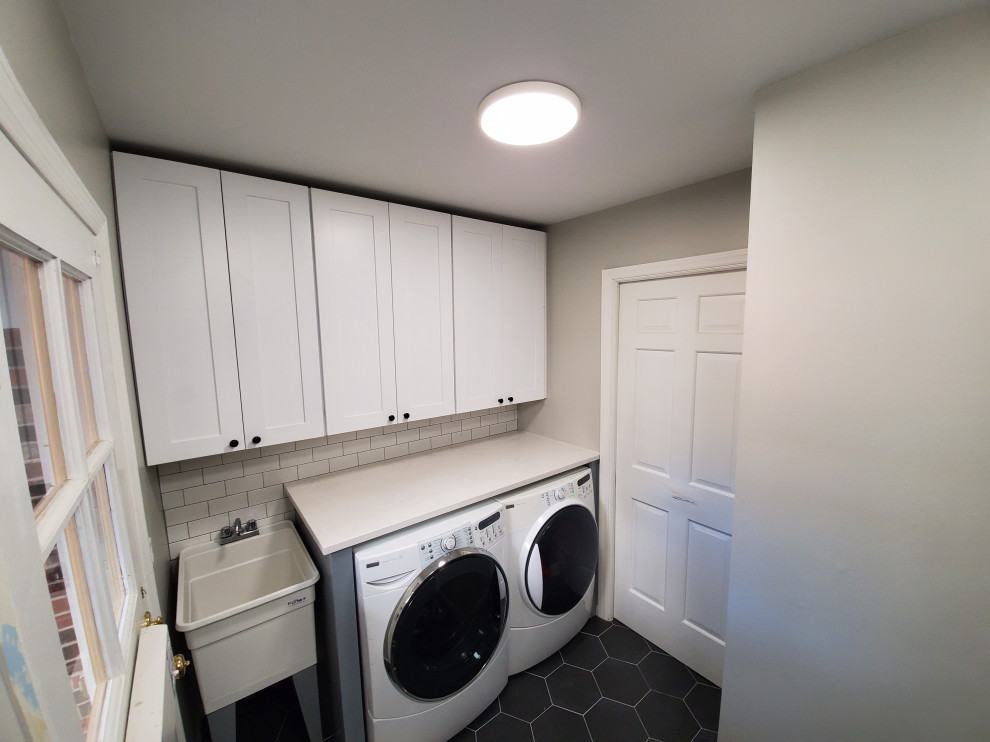 Mid-sized contemporary single-wall utility room in Chicago with an utility sink, shaker cabinets, white cabinets, quartz benchtops, grey walls, porcelain floors, a side-by-side washer and dryer, black floor and white benchtop.