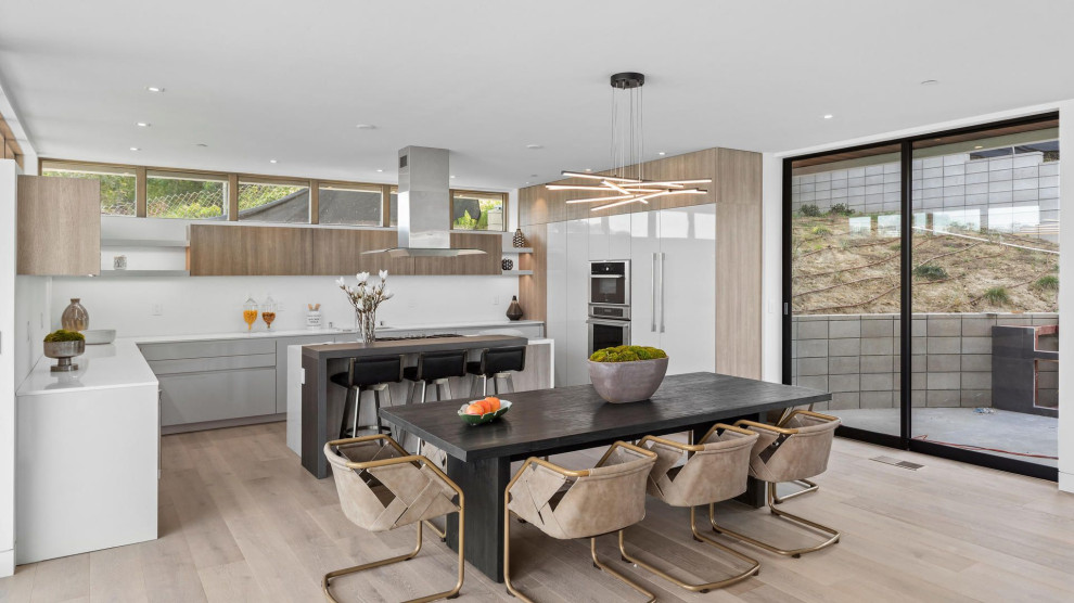 Photo of a mid-sized modern l-shaped eat-in kitchen in San Diego with flat-panel cabinets, grey cabinets, quartz benchtops, white splashback, engineered quartz splashback, stainless steel appliances, light hardwood floors, with island and white benchtop.