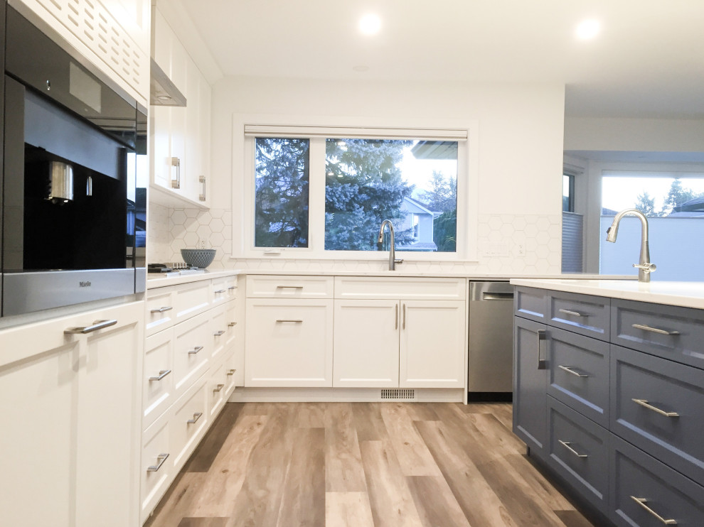 This is an example of a large contemporary l-shaped eat-in kitchen in Vancouver with an undermount sink, flat-panel cabinets, white cabinets, quartz benchtops, white splashback, ceramic splashback, stainless steel appliances, vinyl floors, with island, brown floor and white benchtop.