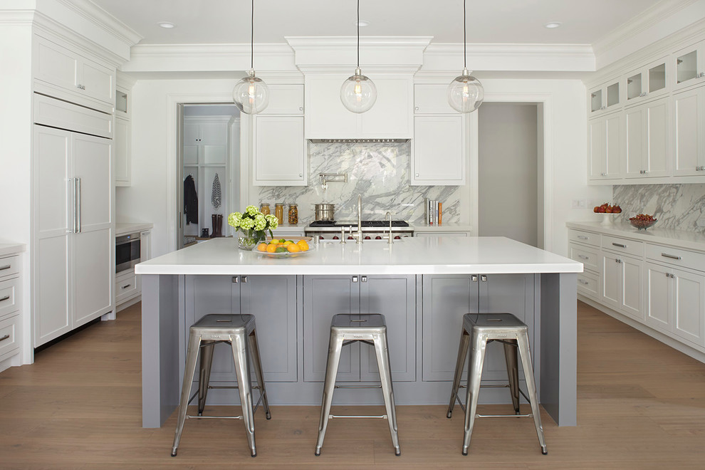 Inspiration for a transitional u-shaped kitchen in San Francisco with shaker cabinets, white cabinets, white splashback, panelled appliances, light hardwood floors, with island and marble splashback.