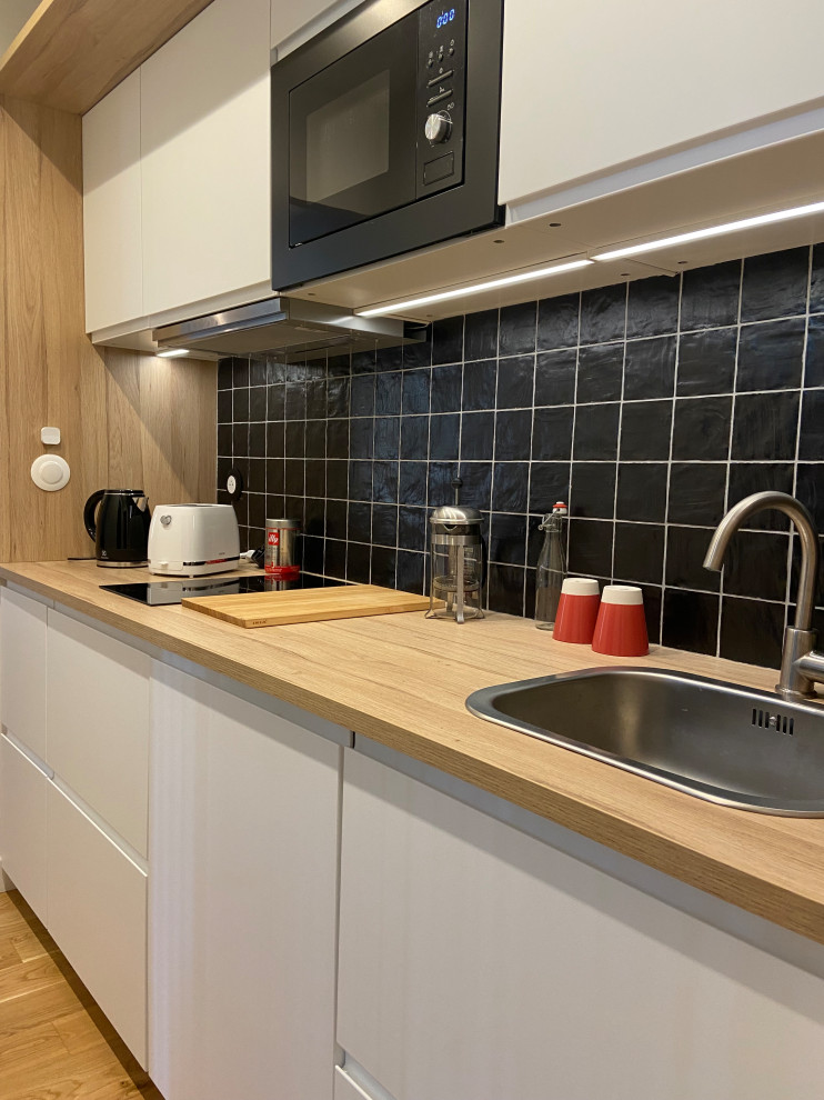 Foto på ett litet funkis linjärt kök, med en enkel diskho, luckor med profilerade fronter, vita skåp, laminatbänkskiva, svart stänkskydd, stänkskydd i skiffer och ljust trägolv