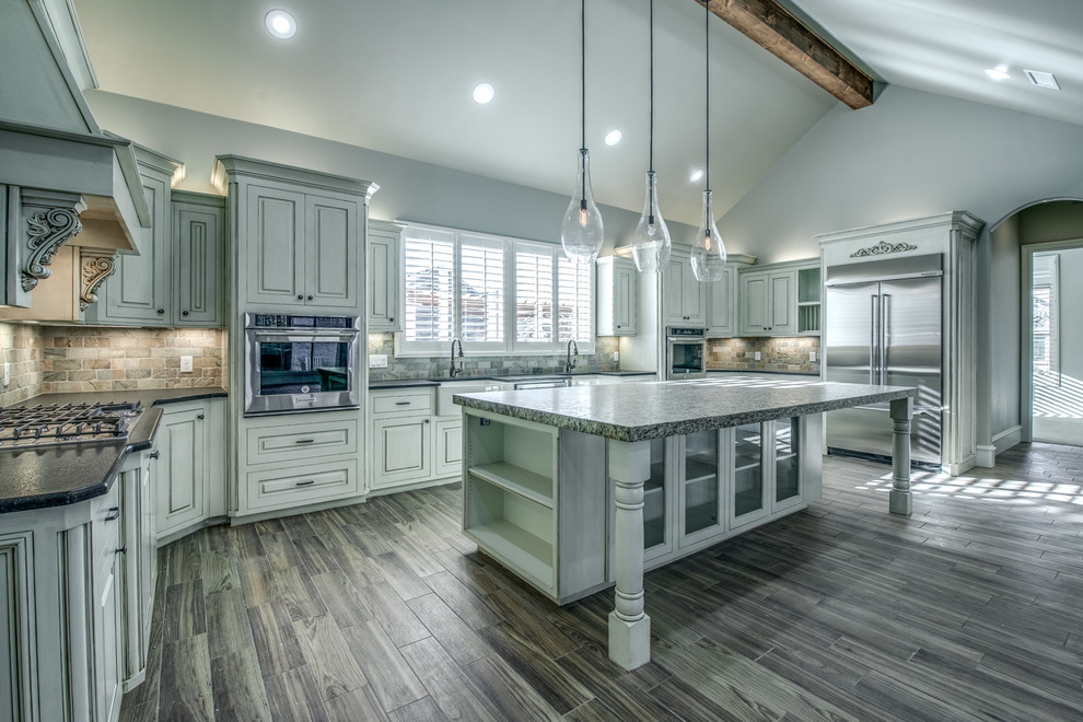 This is an example of a large mediterranean u-shaped kitchen in Austin with a farmhouse sink, raised-panel cabinets, white cabinets, multi-coloured splashback, stone tile splashback, stainless steel appliances, dark hardwood floors, with island and brown floor.
