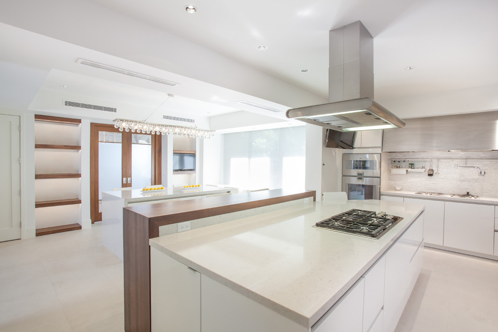 Expansive contemporary u-shaped eat-in kitchen in Houston with a double-bowl sink, flat-panel cabinets, white cabinets, quartz benchtops, white splashback, matchstick tile splashback, stainless steel appliances and multiple islands.