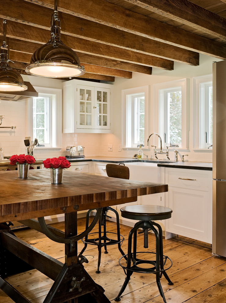 Photo of a country eat-in kitchen in New York with a farmhouse sink, recessed-panel cabinets, white cabinets, white splashback, subway tile splashback, soapstone benchtops and stainless steel appliances.