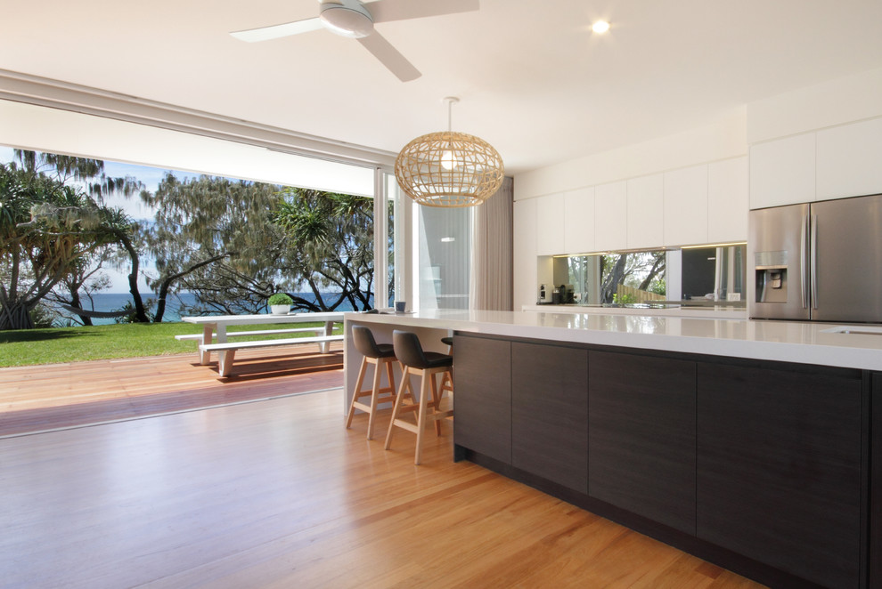 Beach style kitchen in Sunshine Coast with an undermount sink, quartz benchtops, mirror splashback, stainless steel appliances, light hardwood floors and with island.