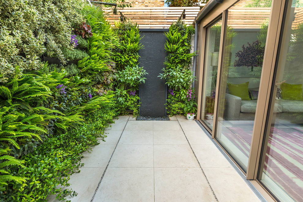 Small contemporary backyard partial sun garden in London with a vertical garden and natural stone pavers for summer.
