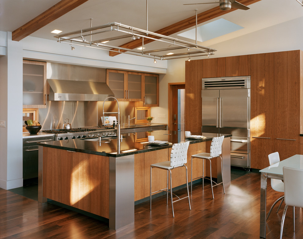 Mid-sized modern l-shaped eat-in kitchen in San Francisco with a double-bowl sink, flat-panel cabinets, medium wood cabinets, granite benchtops, metallic splashback, metal splashback, stainless steel appliances, dark hardwood floors, with island, brown floor, black benchtop and exposed beam.