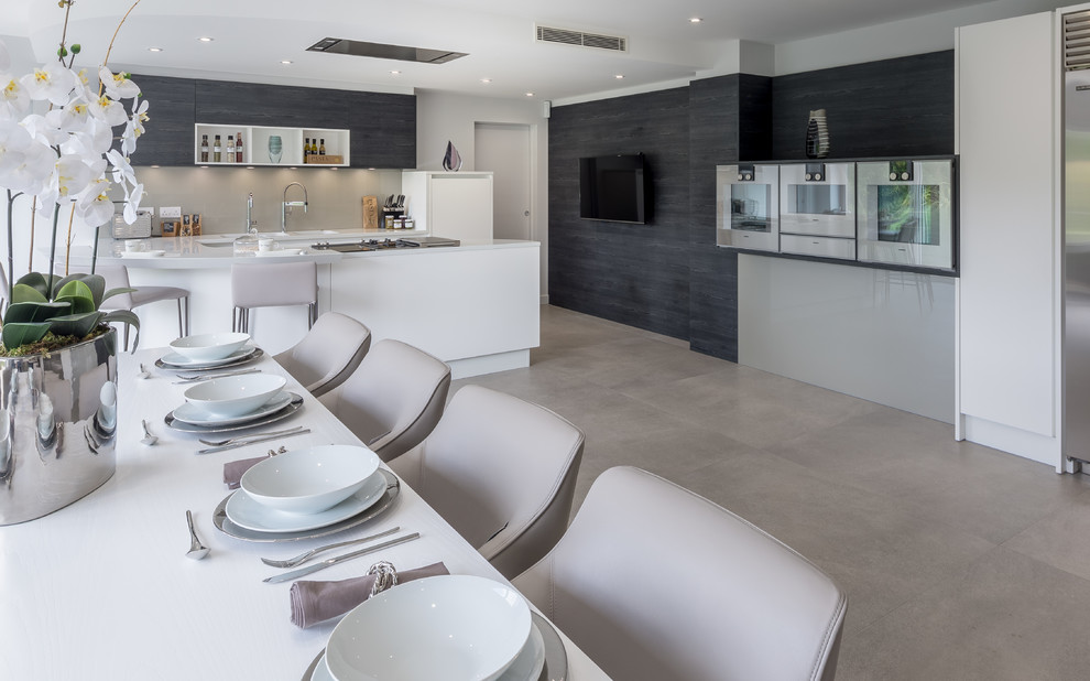 This is an example of a large contemporary u-shaped eat-in kitchen in London with an undermount sink, flat-panel cabinets, white cabinets, quartzite benchtops, grey splashback, glass sheet splashback, stainless steel appliances and a peninsula.